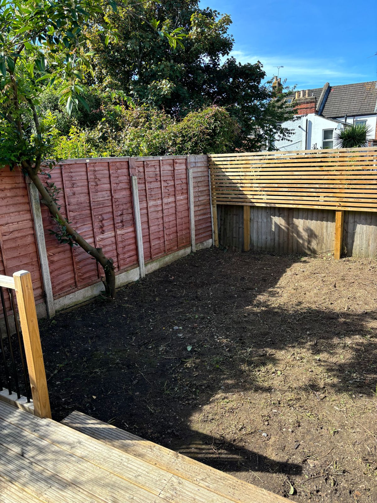 Bare soil and a repaired fence after a garden was stripped.