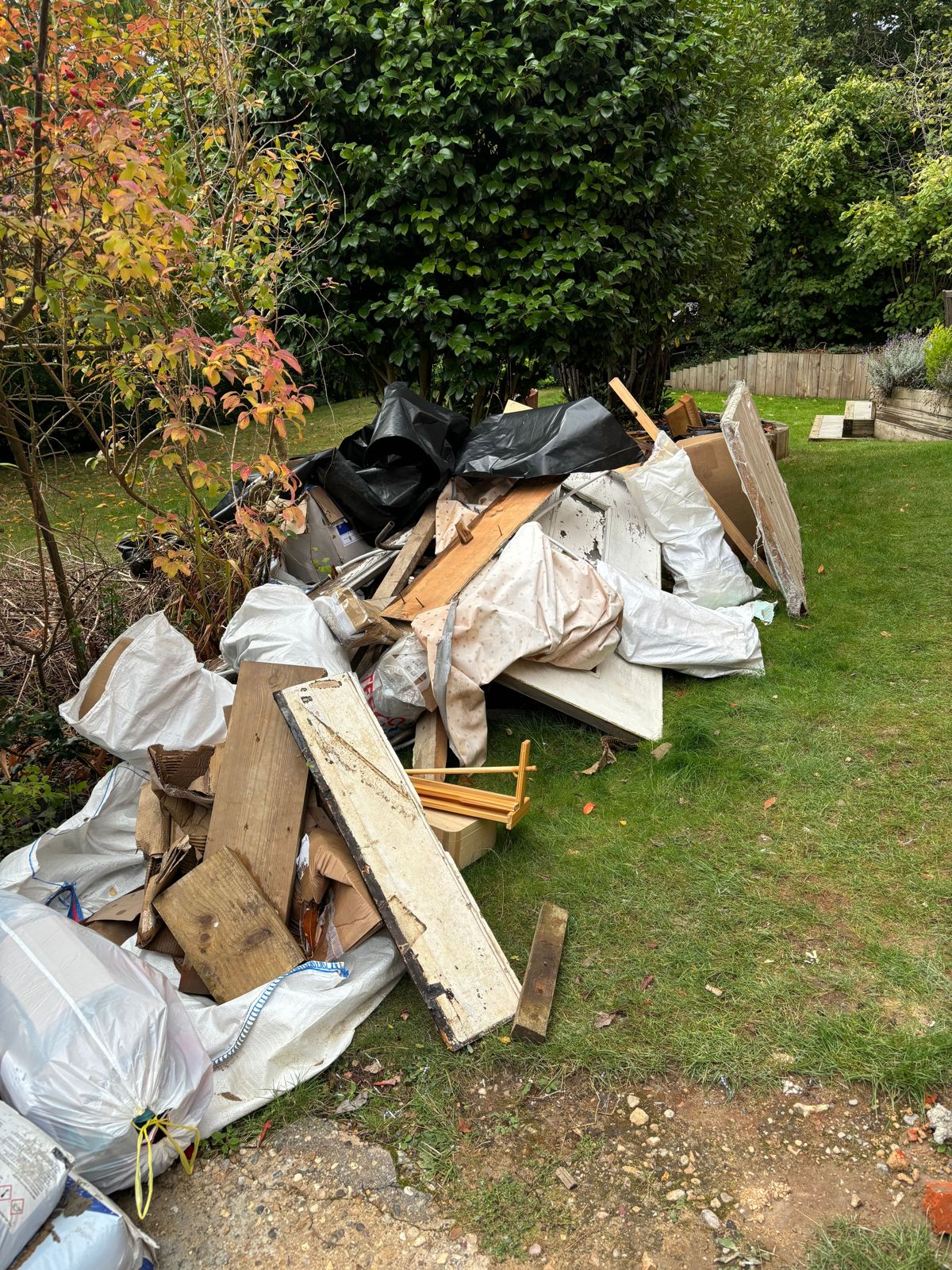 A pile of timber, boards and bagged waste on a lawn, ready to be loaded.